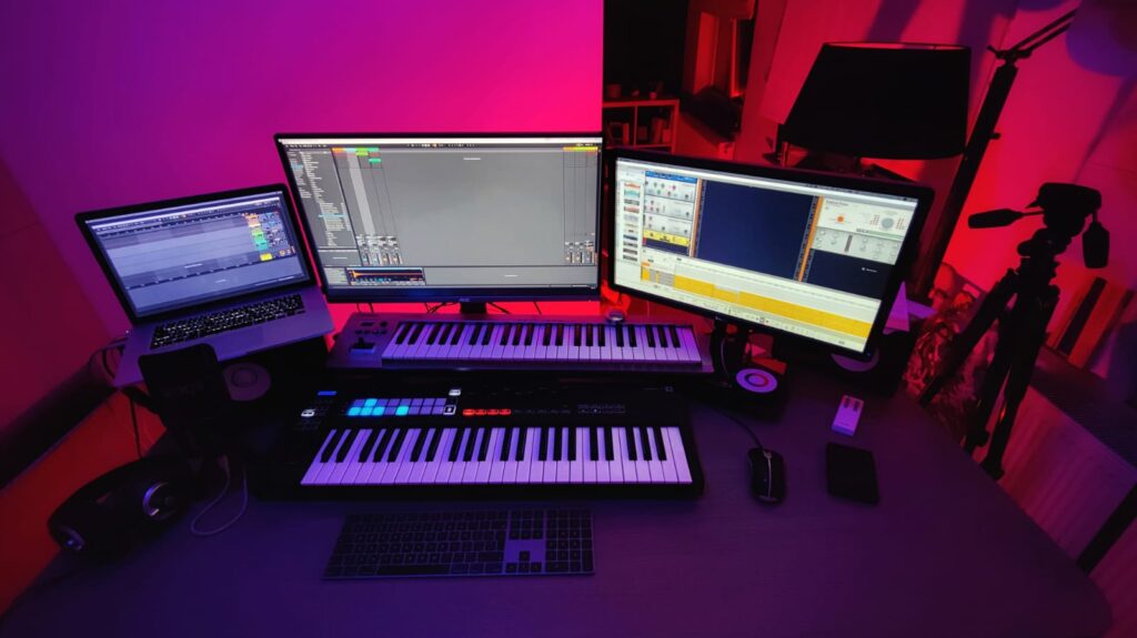 Postazione di produzione musicale con tastiere, controller e monitor in luce viola